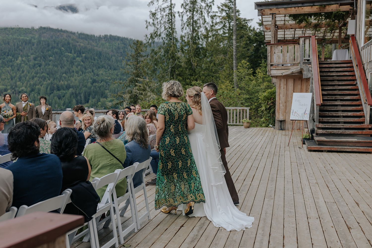 Panoramic view of mountain wedding venue with guests on spacious wooden deck.