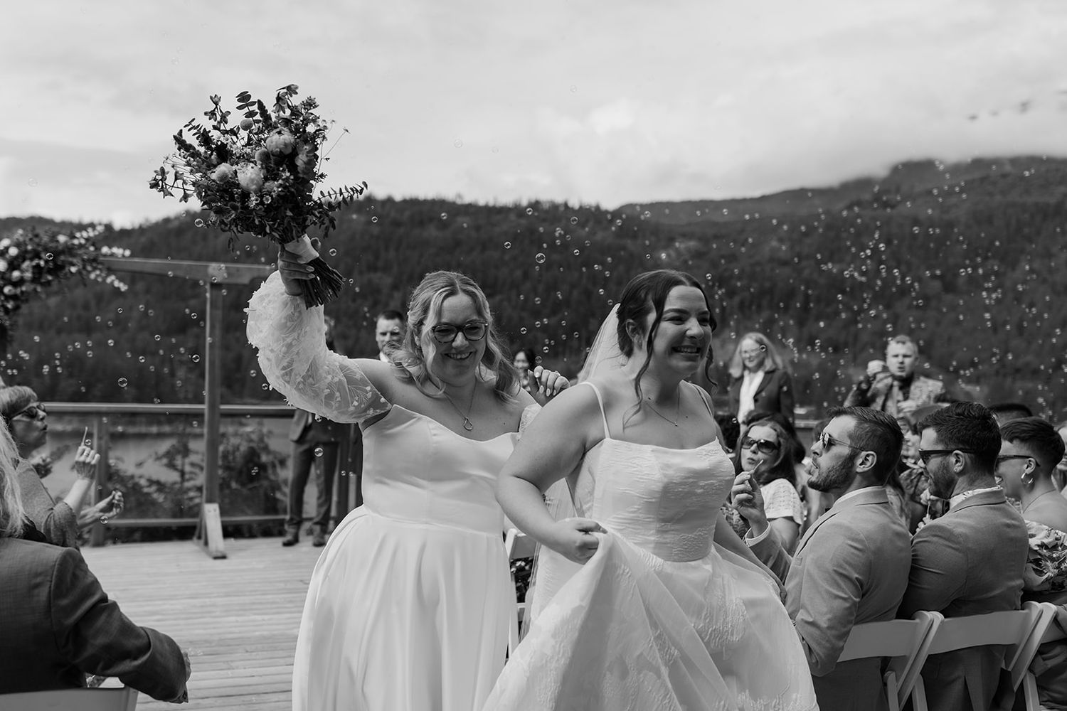 Wedding guests blow bubbles during an outdoor mountain celebration.
