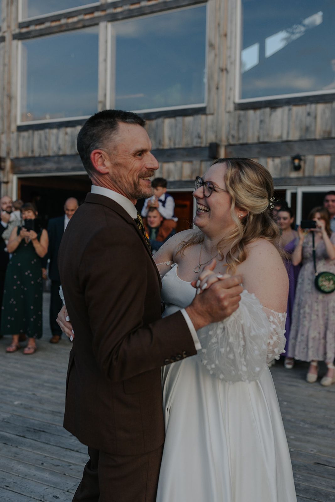 Wedding dance taking place on a wooden deck with guests looking on.