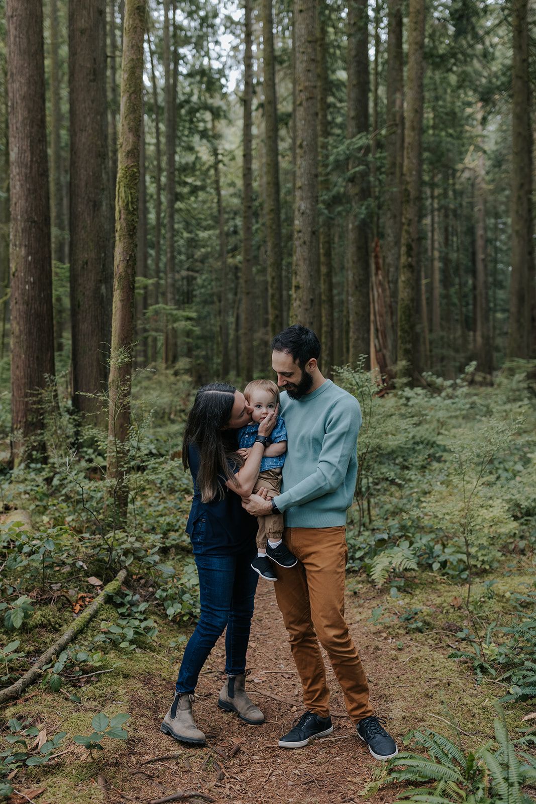 Family sharing intimate moments together on a forest trail surrounded by tall trees.