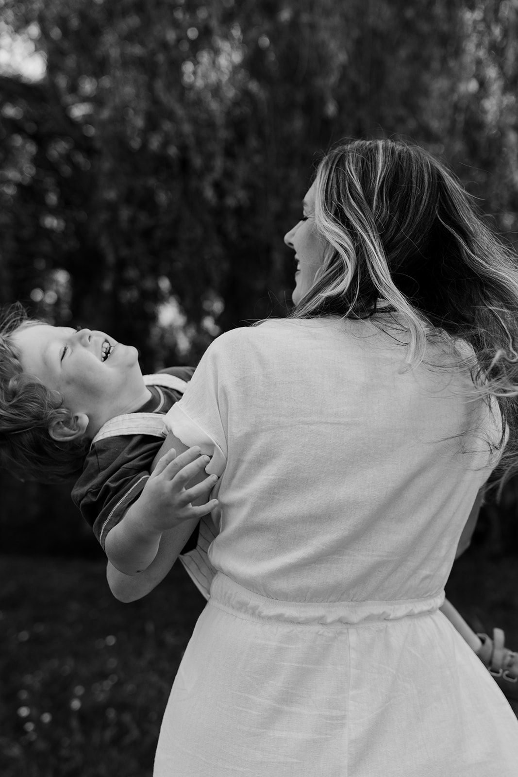 A candid black and white photo captures a joyful moment between parent and child outdoors.