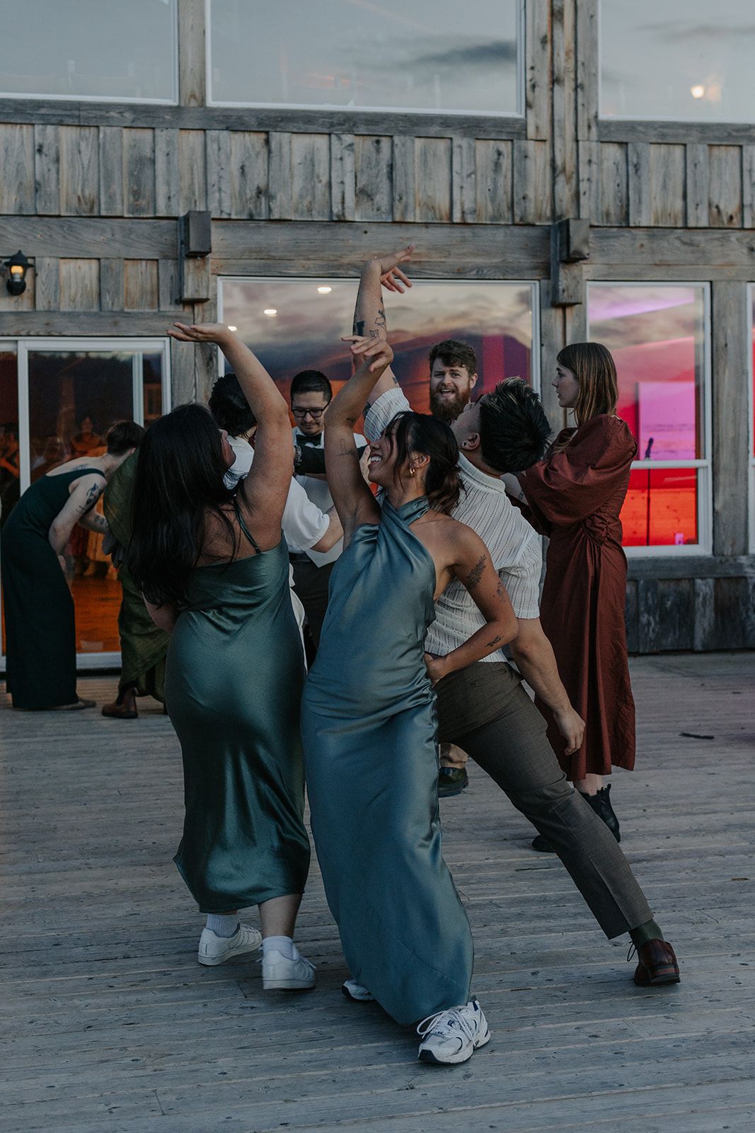 Group performs synchronized dance moves on a wooden deck at dusk.