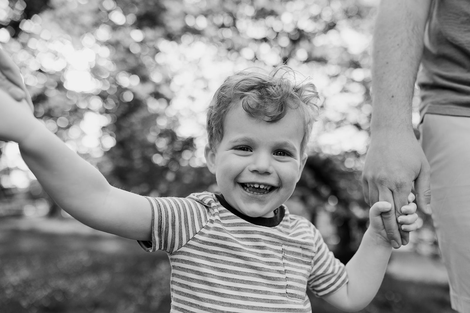 Black and white portrait of a joyful child with arms outstretched wearing a striped shirt.
