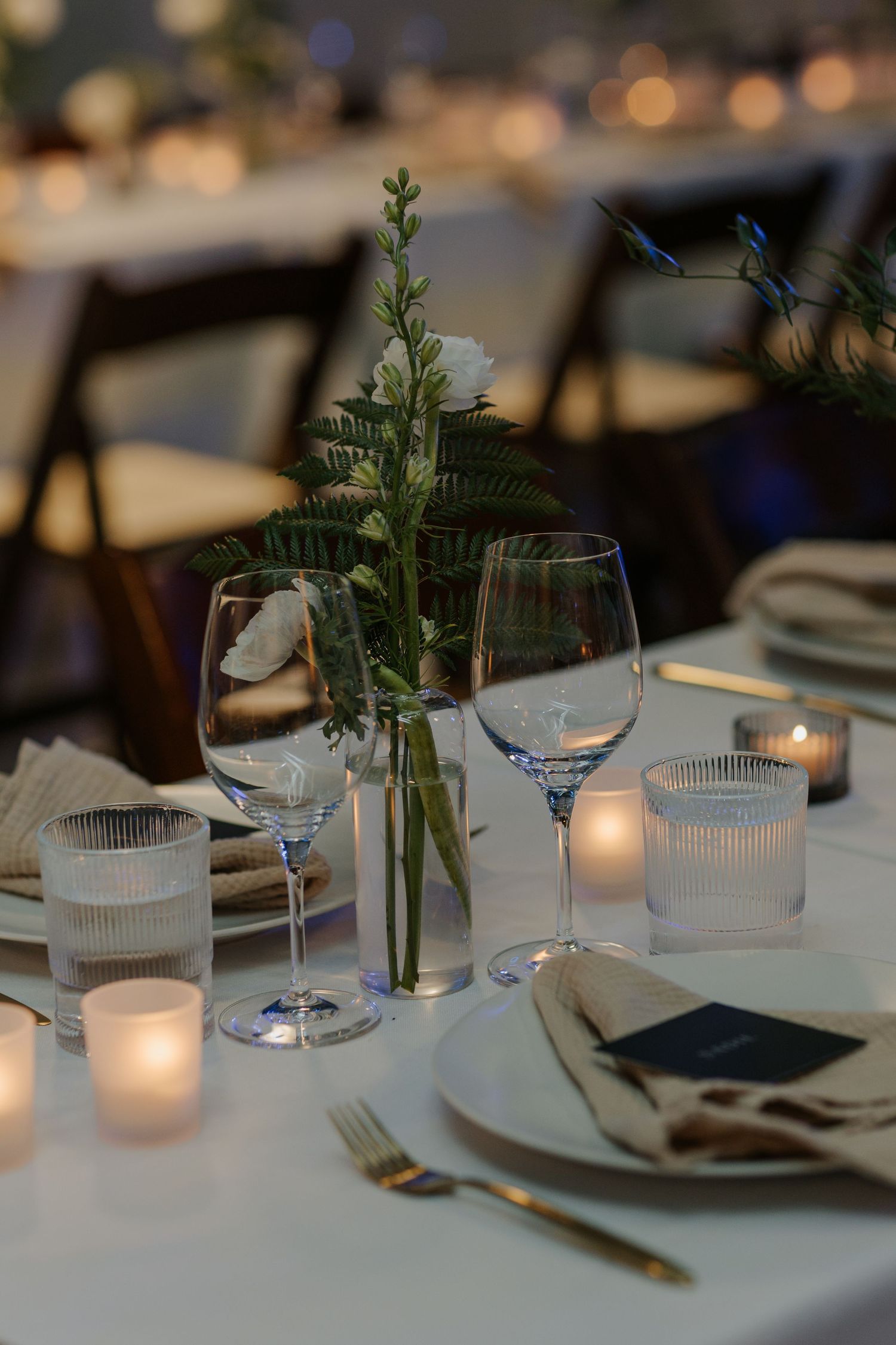 Elegant table settings with white candles, greenery and navy accents at wedding reception.