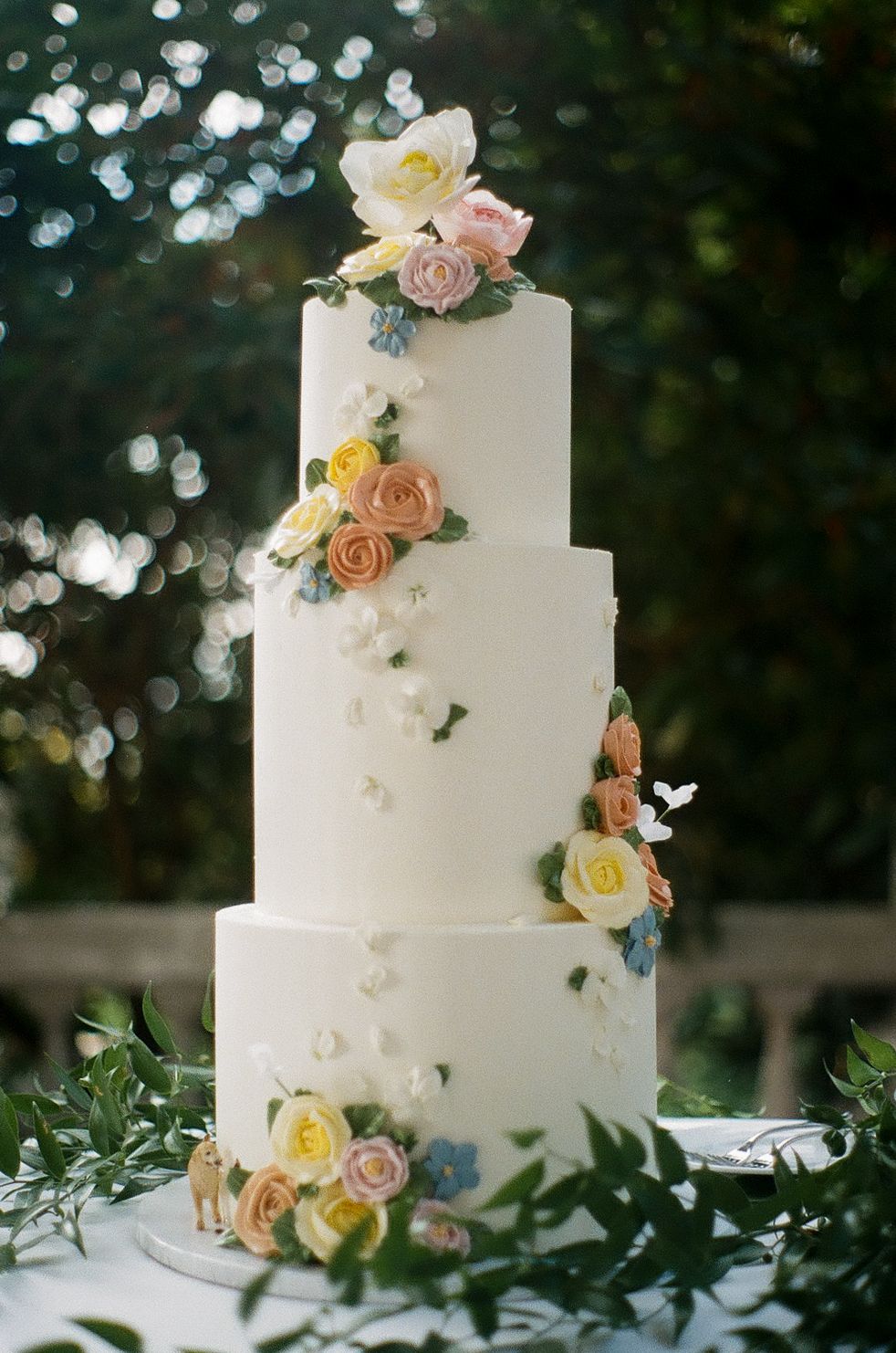 Elegant white tiered wedding cake decorated with pastel roses and eucalyptus leaves.