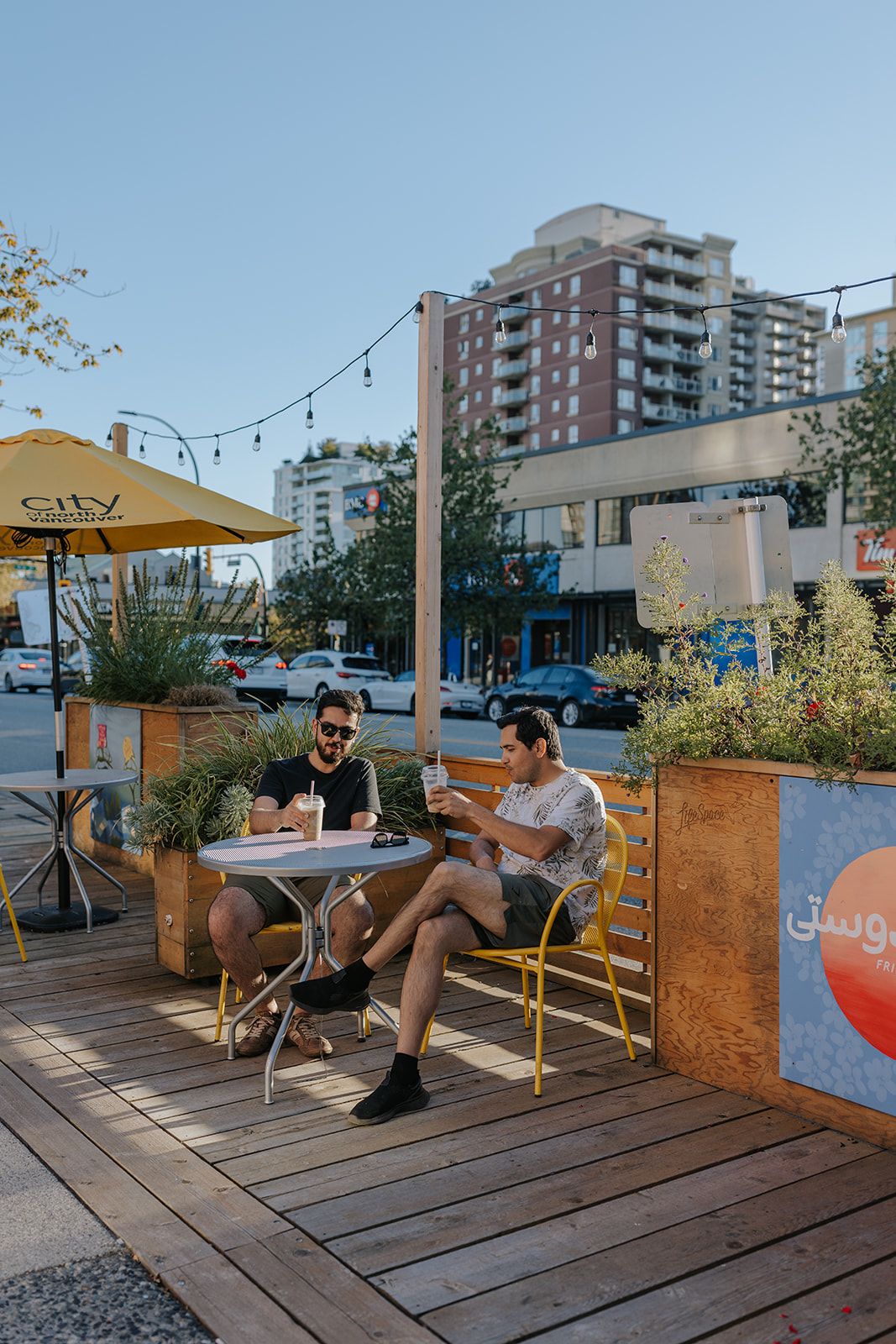 Modern rooftop patio with wooden decking, yellow umbrellas and planters against urban apartment buildings.