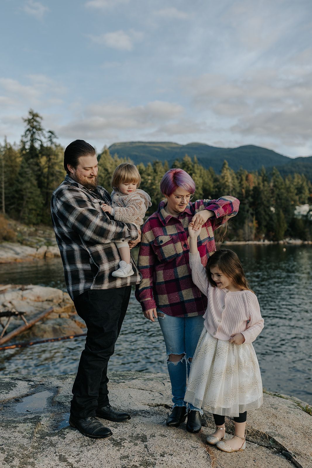 Family photoshoot on rocky coastline with mountains and water in the background.