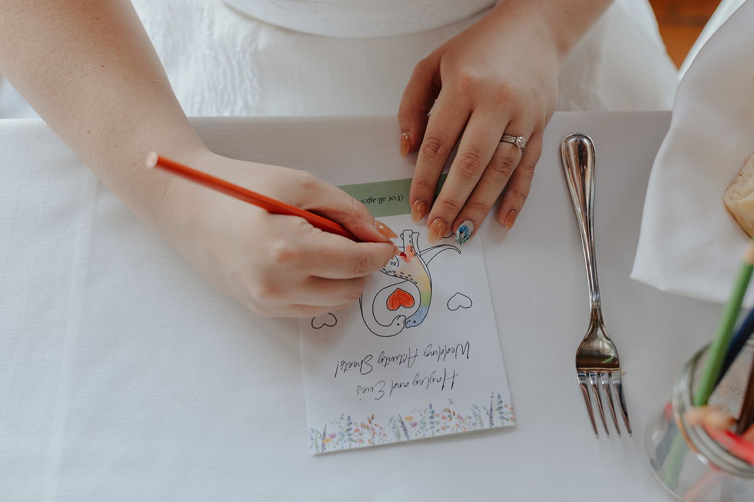 Hands writing on white paper at a formal dining table setting.