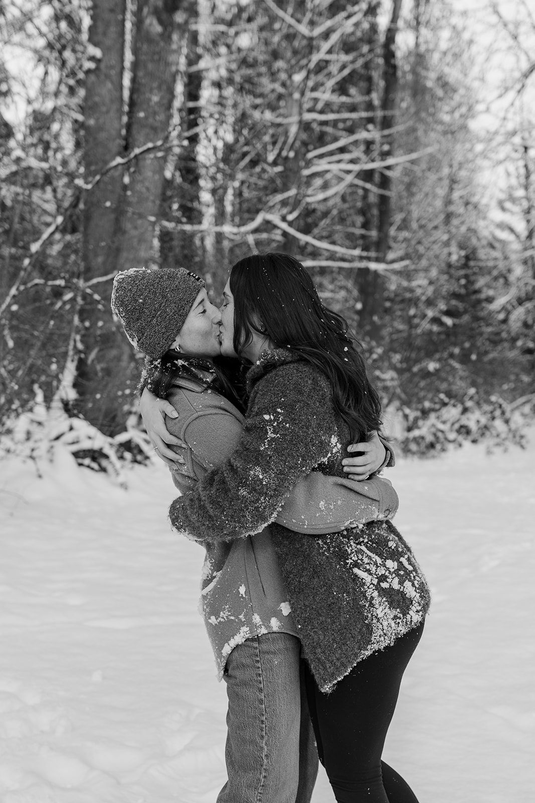 Two people playfully throw snow at each other in a winter forest setting.