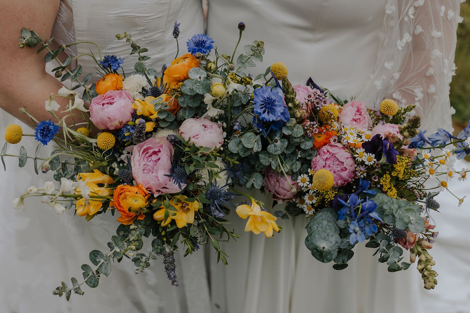 Close-up of vibrant wedding bouquets featuring pink, blue, and yellow flowers with greenery.