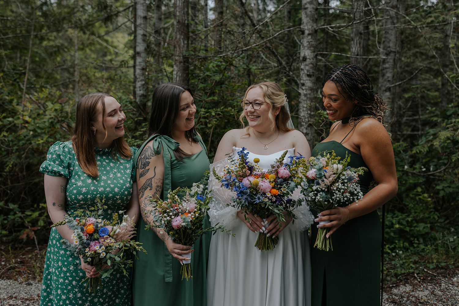 Wedding party in green dresses holding colorful bouquets in a forest setting.