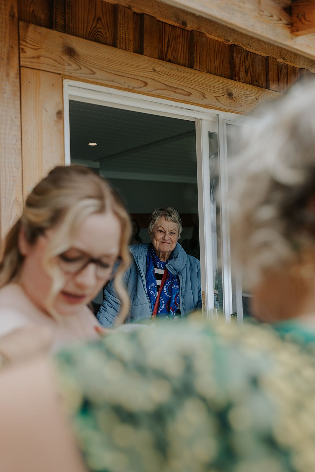 Wedding preparation scene through window with green floral dresses visible.