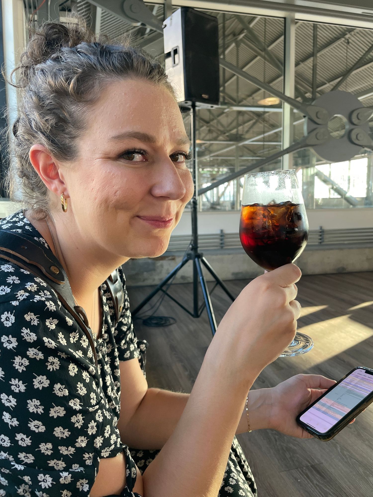 Woman in floral print enjoying wine while checking phone at outdoor patio.