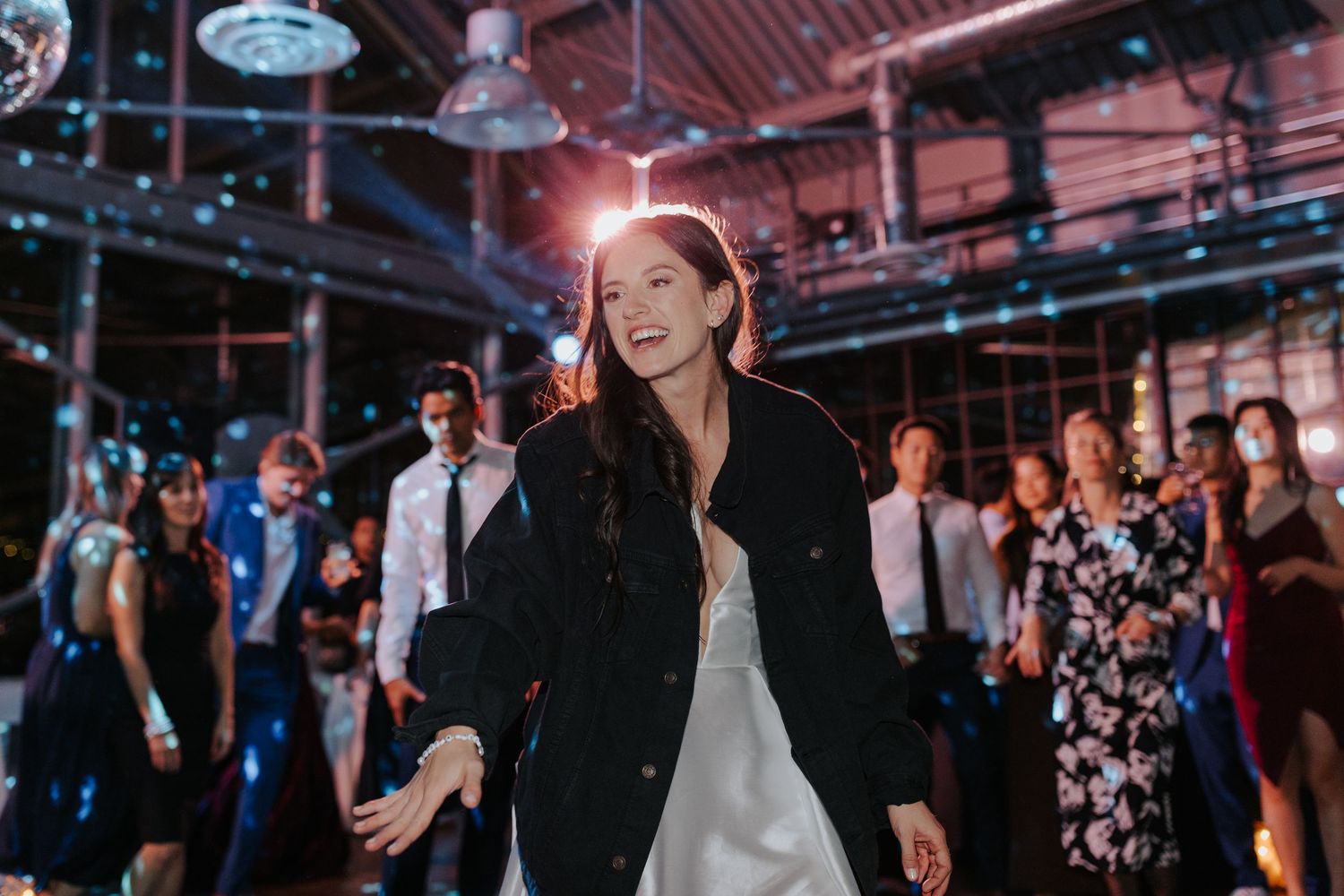 Wedding reception venue with pink lighting and guests mingling on the dance floor.