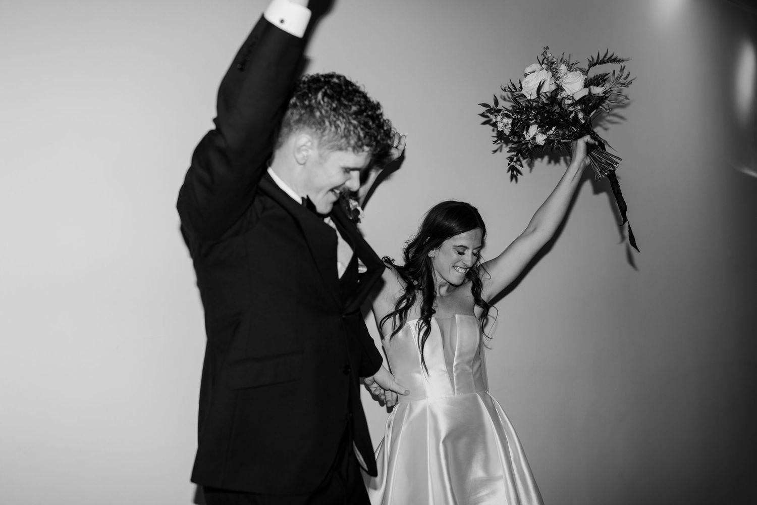 Black and white photo of wedding couple celebrating with dramatic lighting.