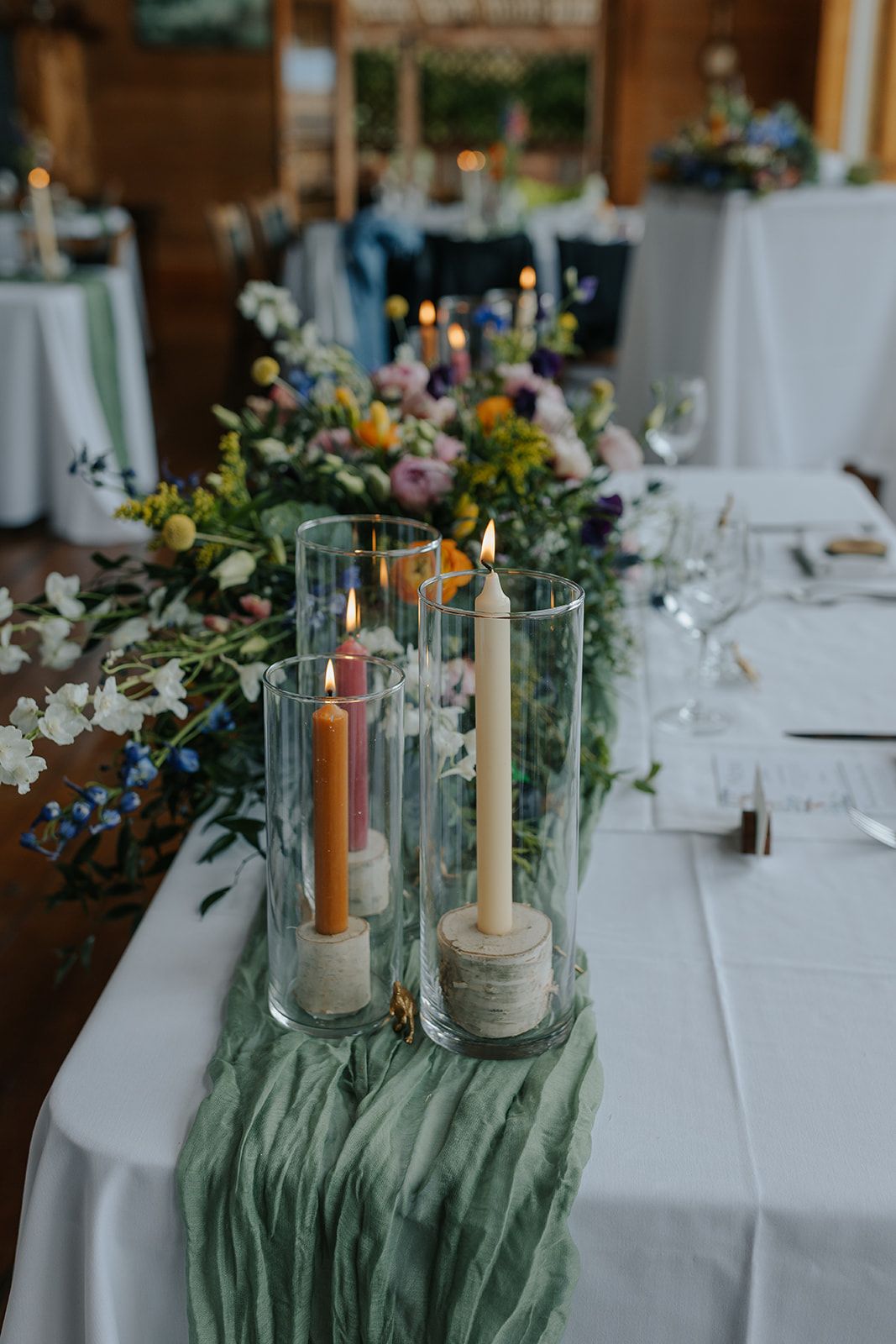 Elegant wedding table decor with candles, greenery and colorful flower arrangements.