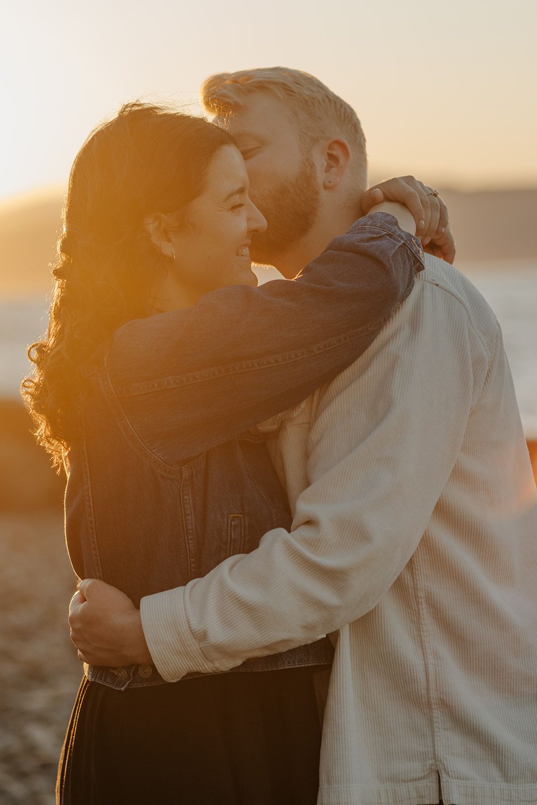 A couple embraces during golden hour sunset with warm backlighting creating a romantic silhouette.