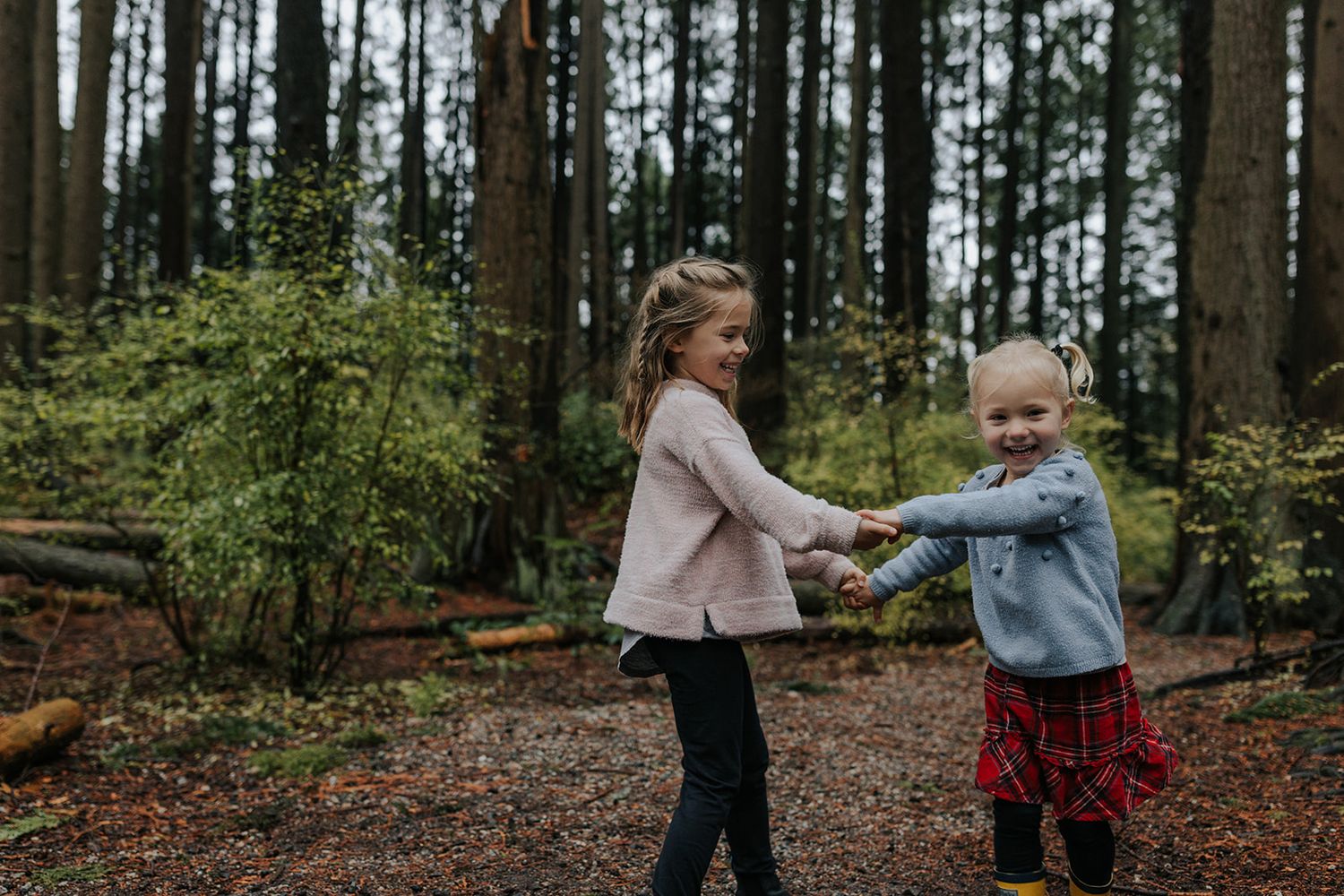 Two children playing and holding hands while exploring a forest trail.