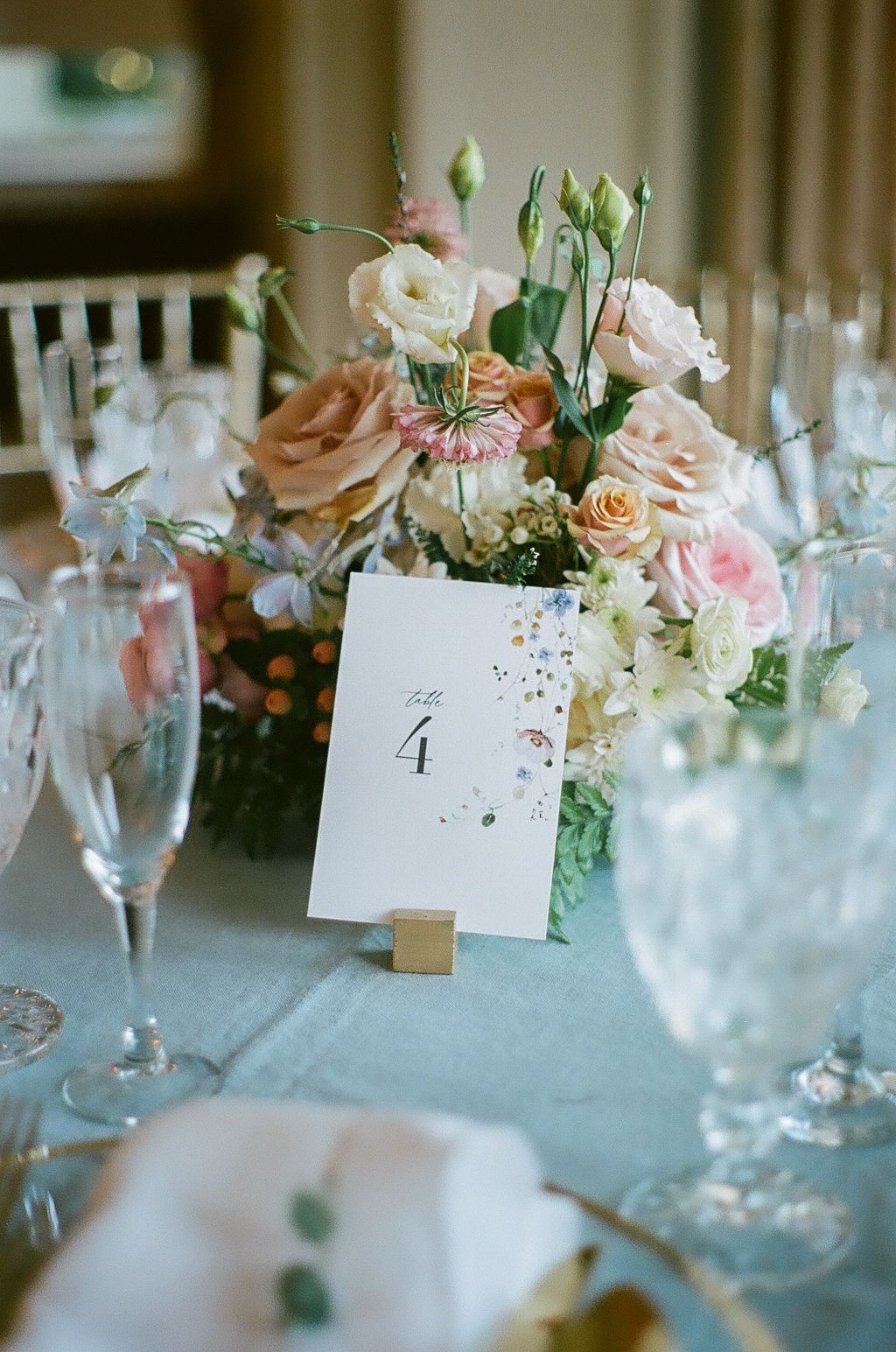 Elegant wedding table setting with pink and peach roses, delicate glassware, and table number cards.