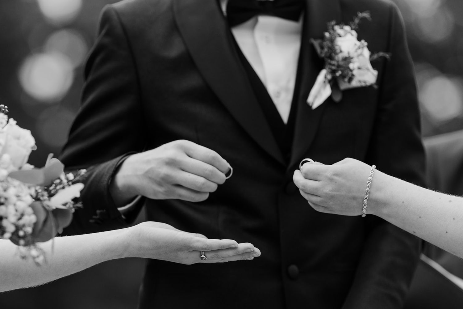 Close-up black and white shots of hands exchanging wedding rings during a ceremony.
