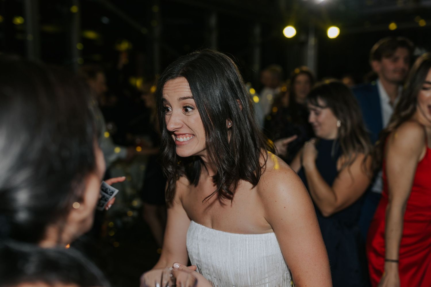 A guest in a white dress engages in animated conversation during an evening reception.