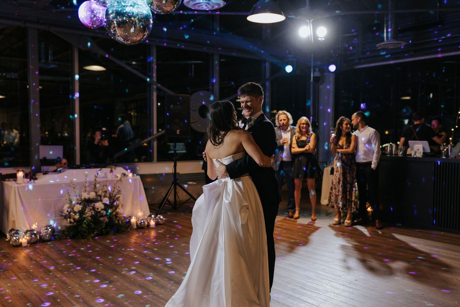 Newlyweds share their first dance under disco balls in a dimly lit reception venue.