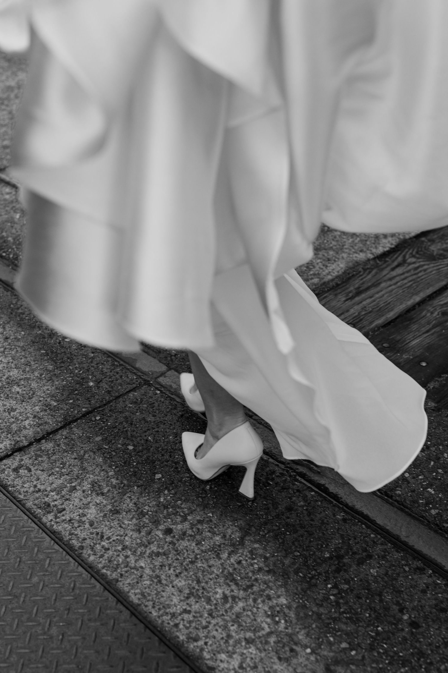 Close-up of white wedding dress and heels on textured ground during bridal photoshoot.