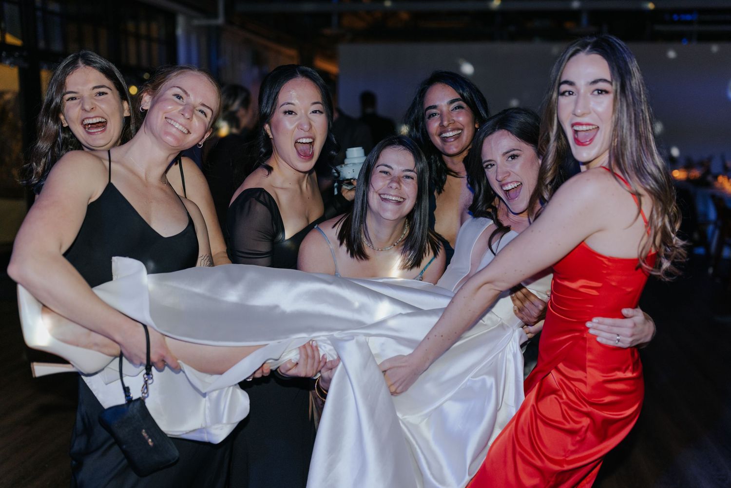Group of wedding guests in red and white dresses celebrating on the dance floor.
