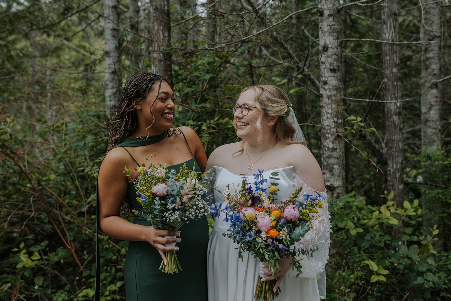 Joyful candid moments between wedding party members holding vibrant bouquets in forest setting.