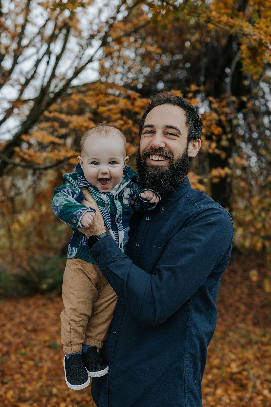 Father and baby laughing together against autumn foliage background.