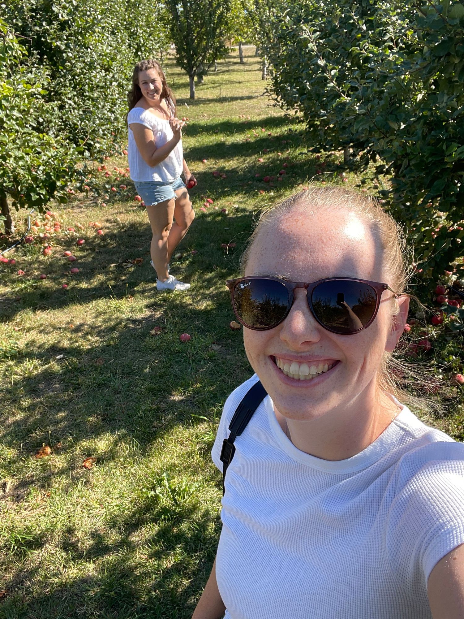 Woman in white shirt smiling while enjoying sunny day in apple orchard.