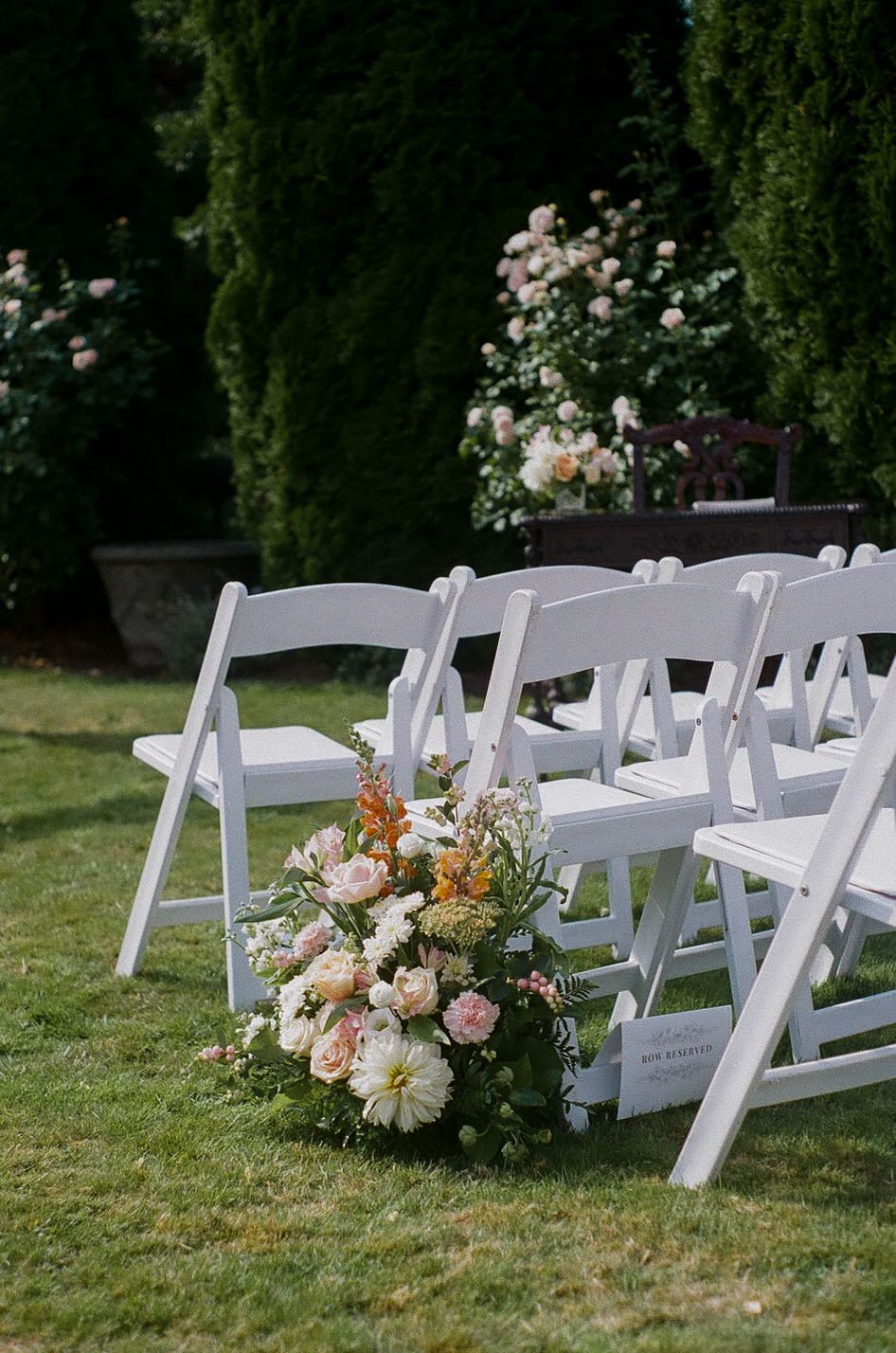 White folding chairs arranged for an outdoor wedding ceremony with elegant floral arrangements on a manicured lawn.