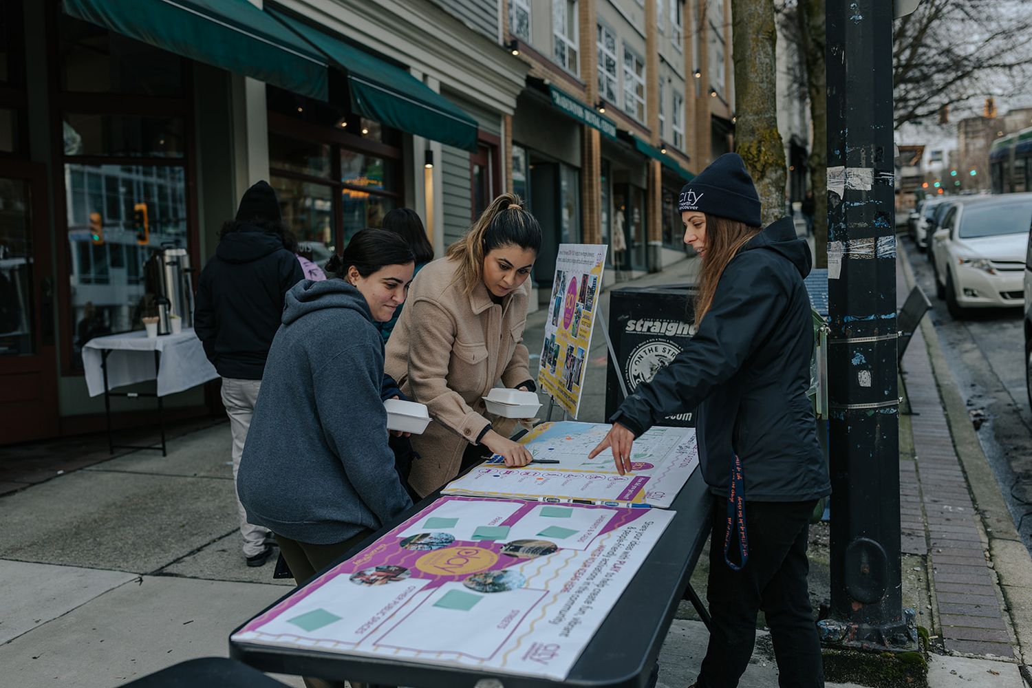 People gathered around a table on an urban street discussing documents.