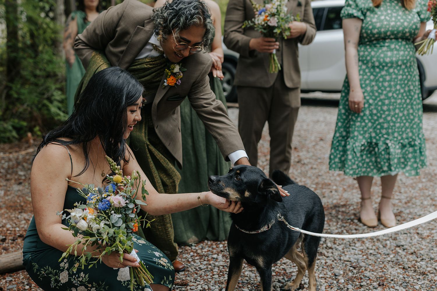 Black dog interacting with wedding party members in a forest setting.