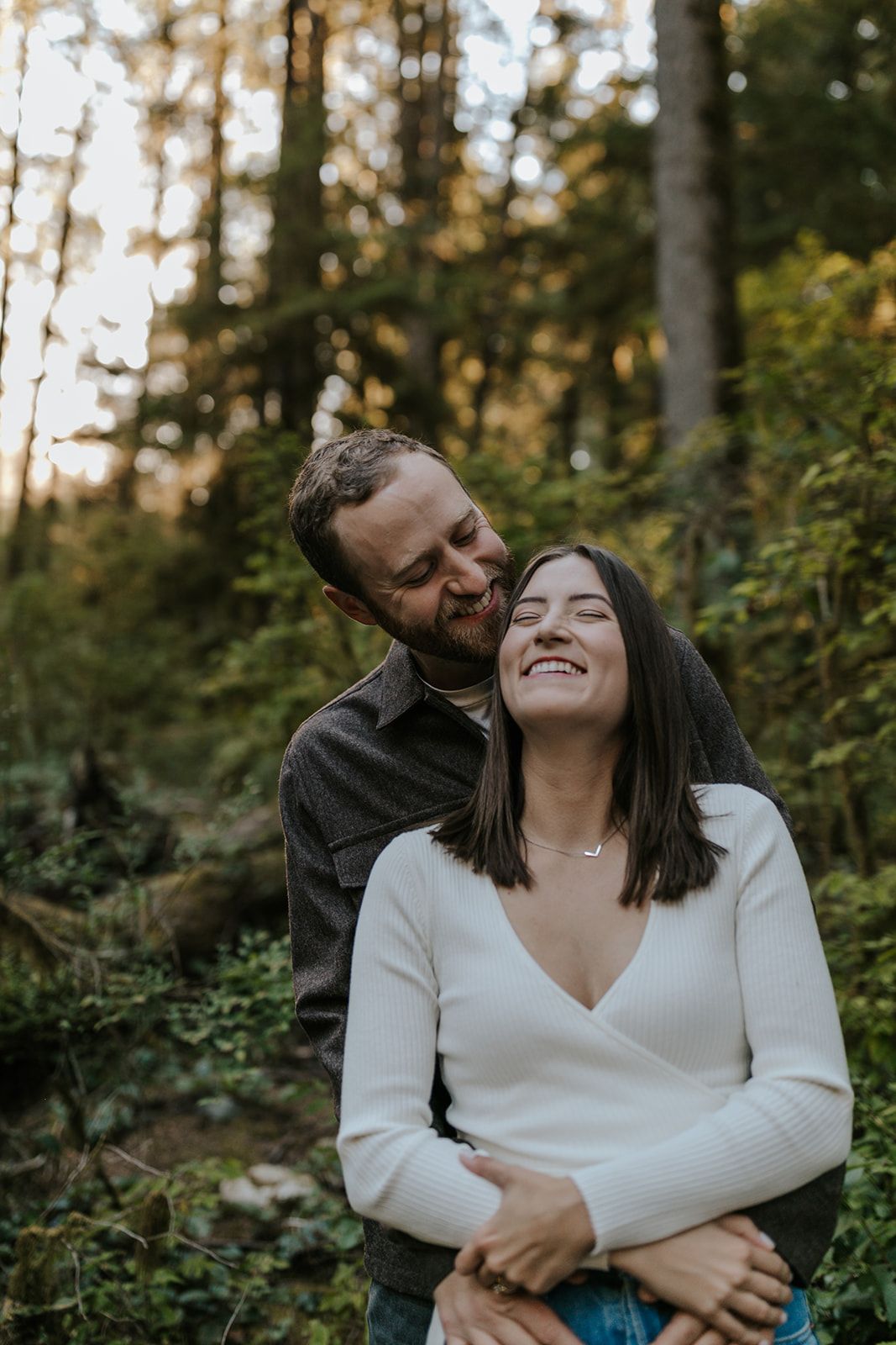 A candid moment of laughter and embrace among tall trees at sunset.
