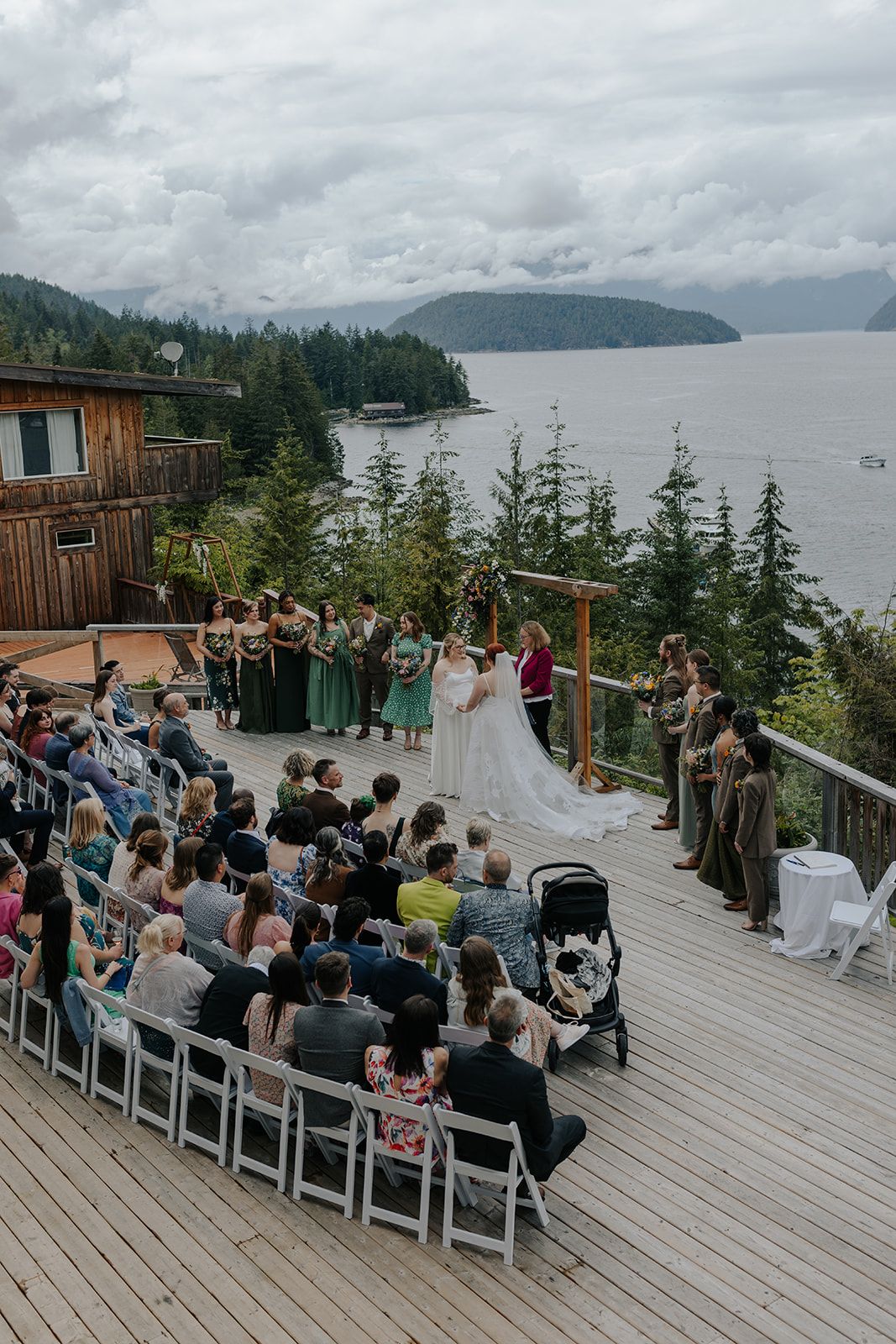 Wedding ceremony setup on waterfront deck with mountain views and seated guests.