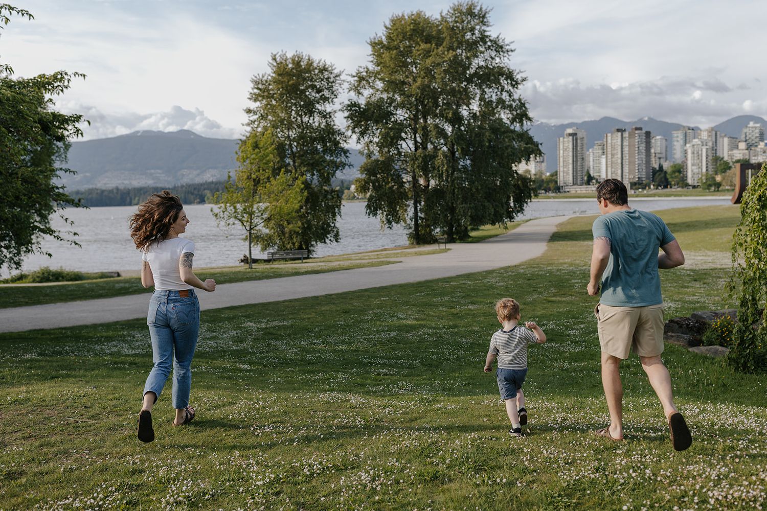 Family walking together on grassy path with mountains and water in background.