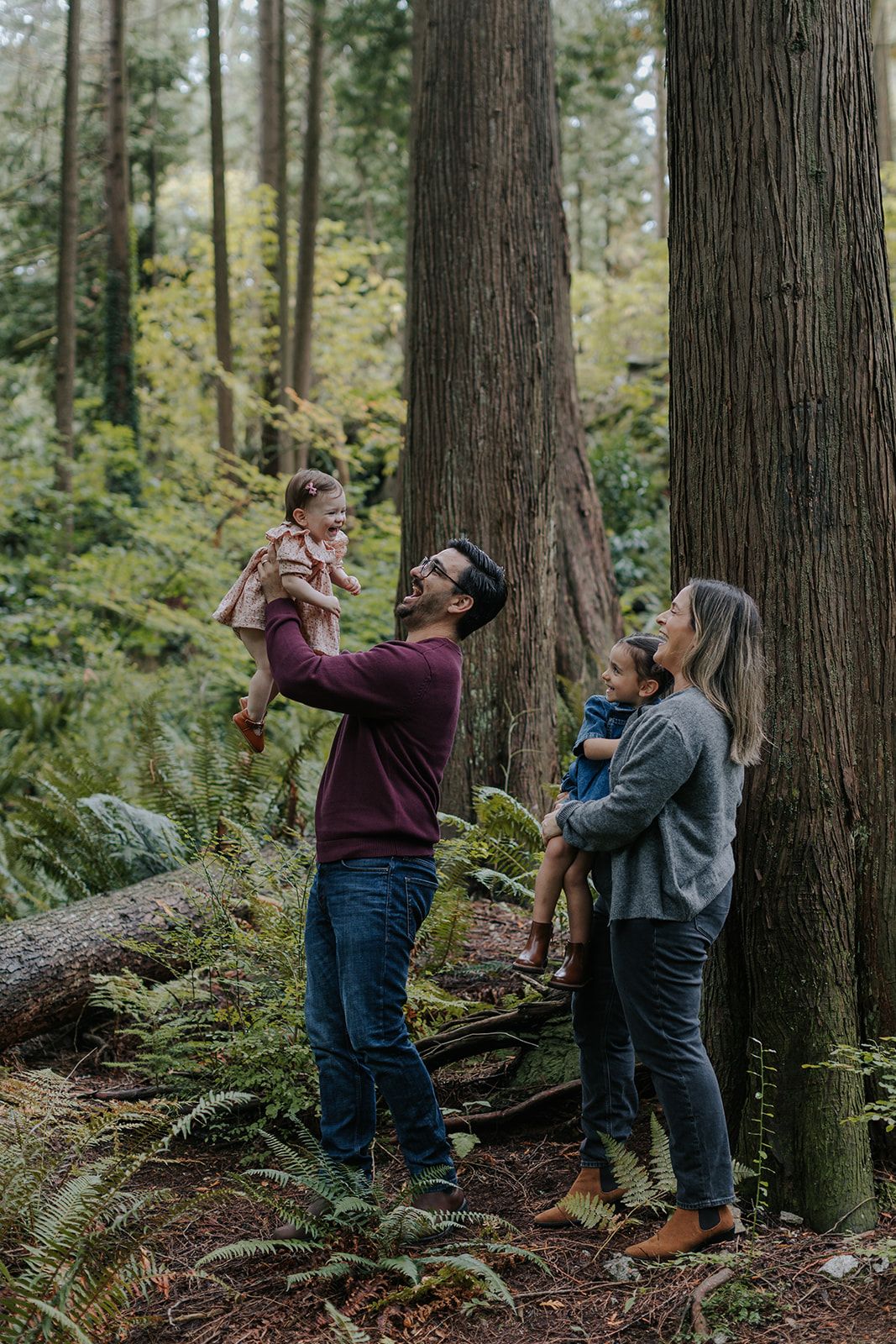 Family playing and dancing together among tall trees in a mossy forest.