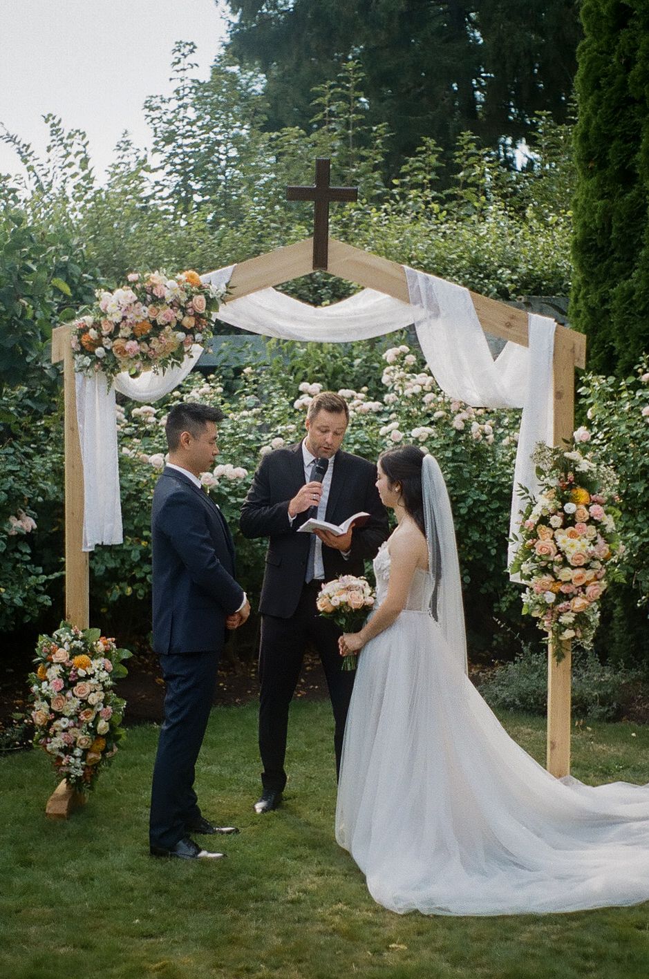 Wooden wedding arch decorated with peach and white flowers during an outdoor garden ceremony.