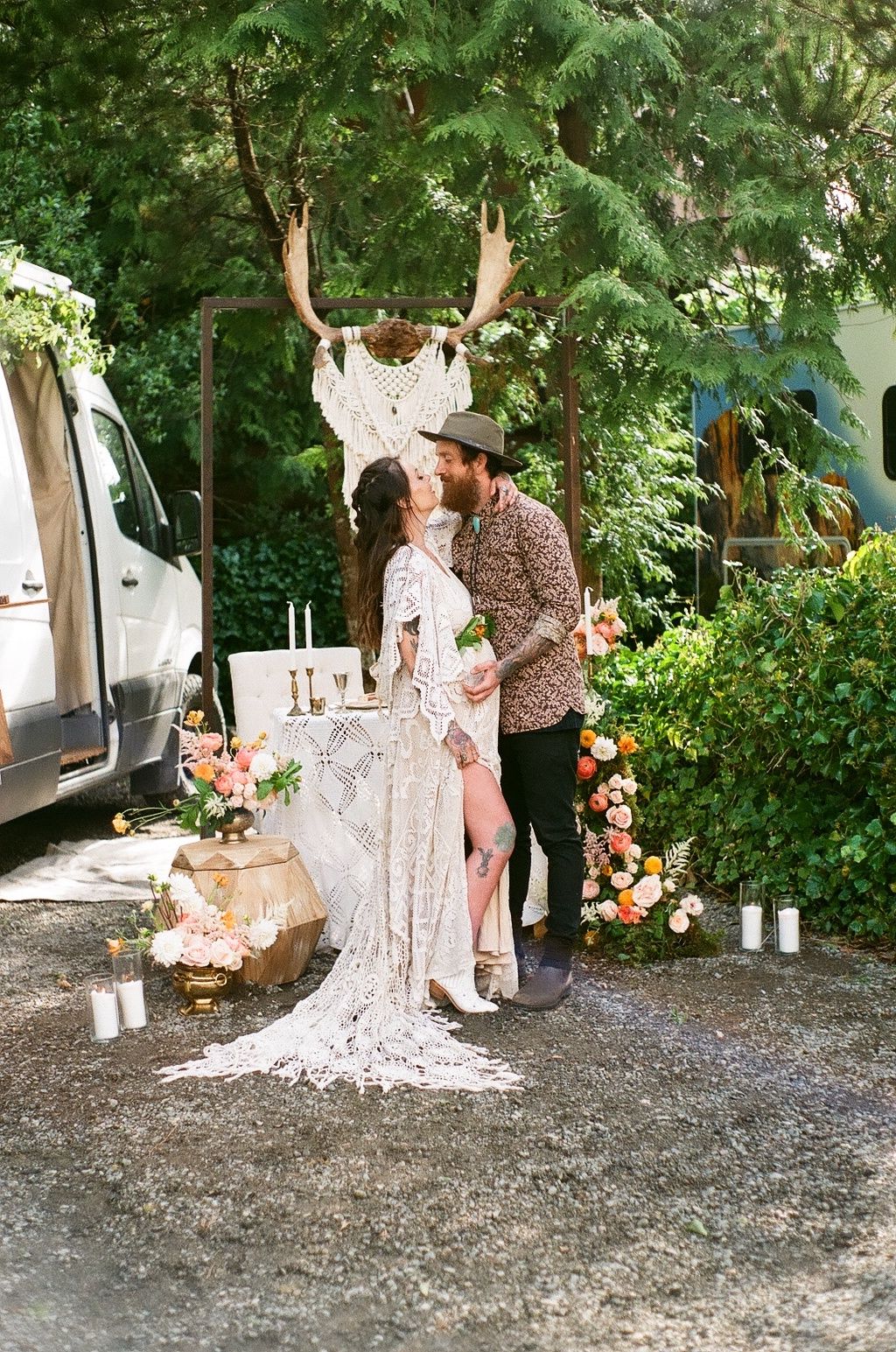 Romantic couple poses beside a decorated van with macrame and floral arrangements.