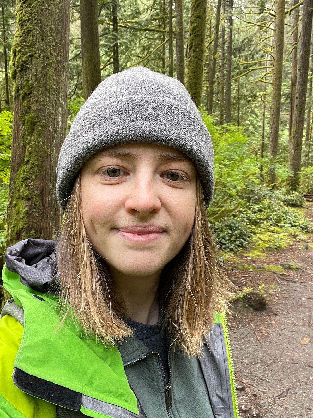 A series of selfies taken in a forest wearing a gray beanie and neon green jacket.