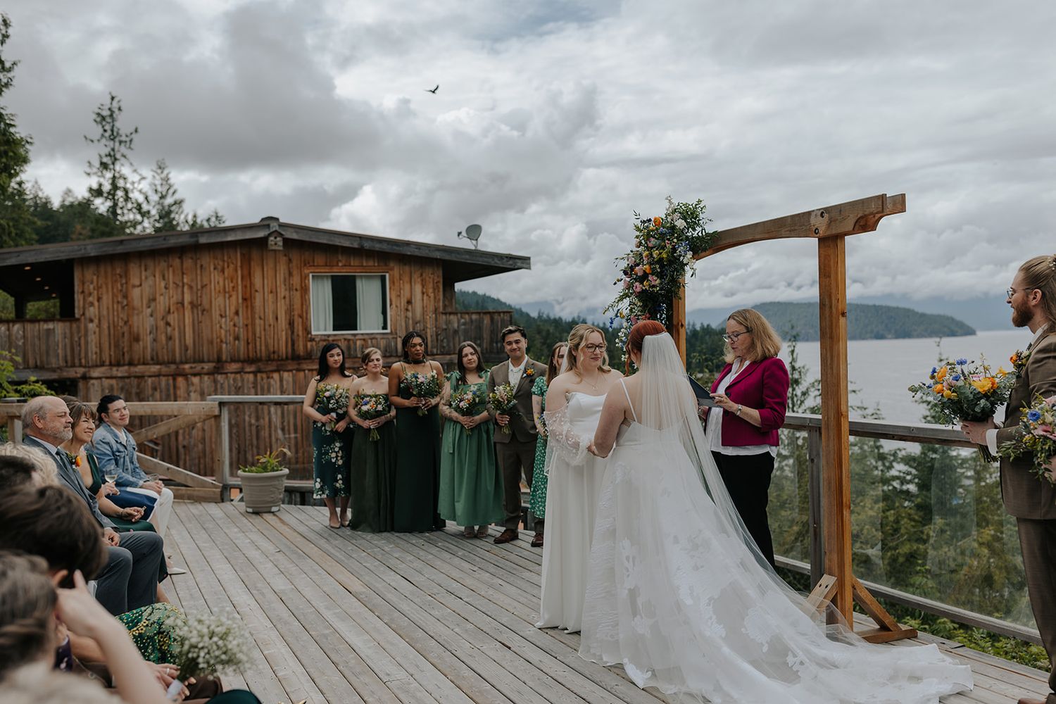 Wedding guests seated on a rustic wooden deck with mountain and lake views in the background.