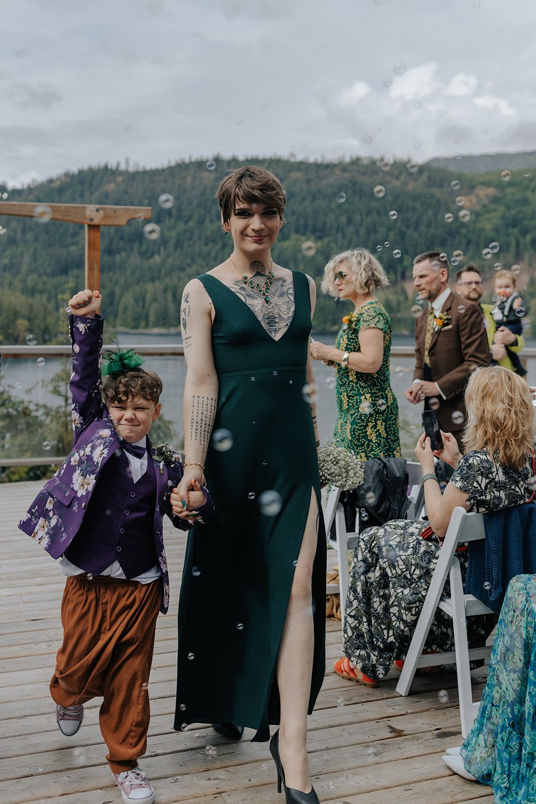 Wedding celebration with guests dancing in colorful attire on lakeside deck.
