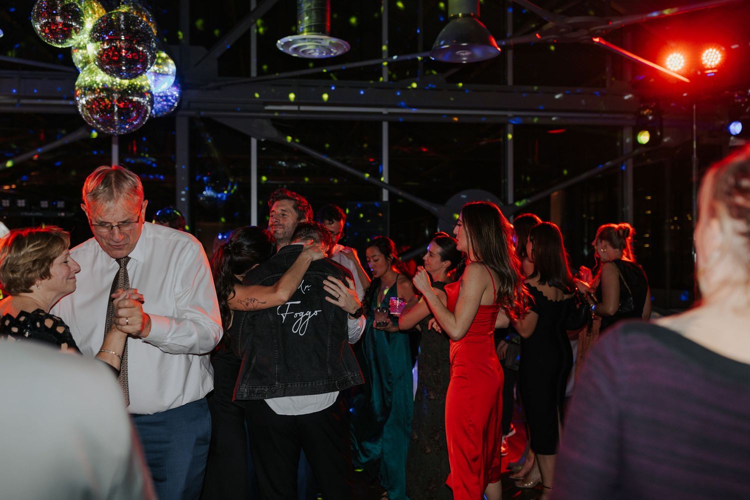 Wedding guests celebrating on dance floor under colorful disco lights.