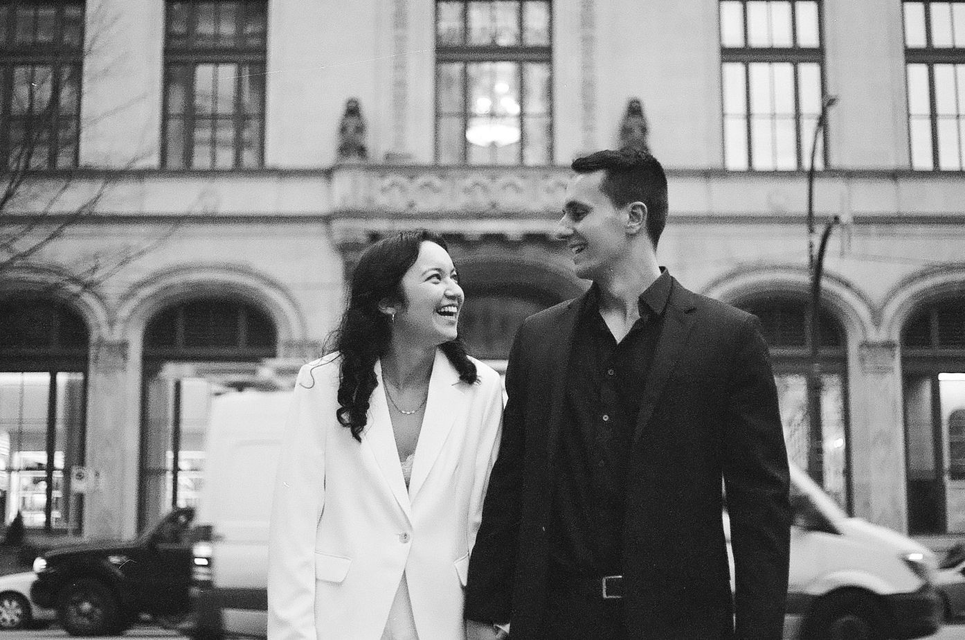 A joyful couple laughs together outside a classic building.
