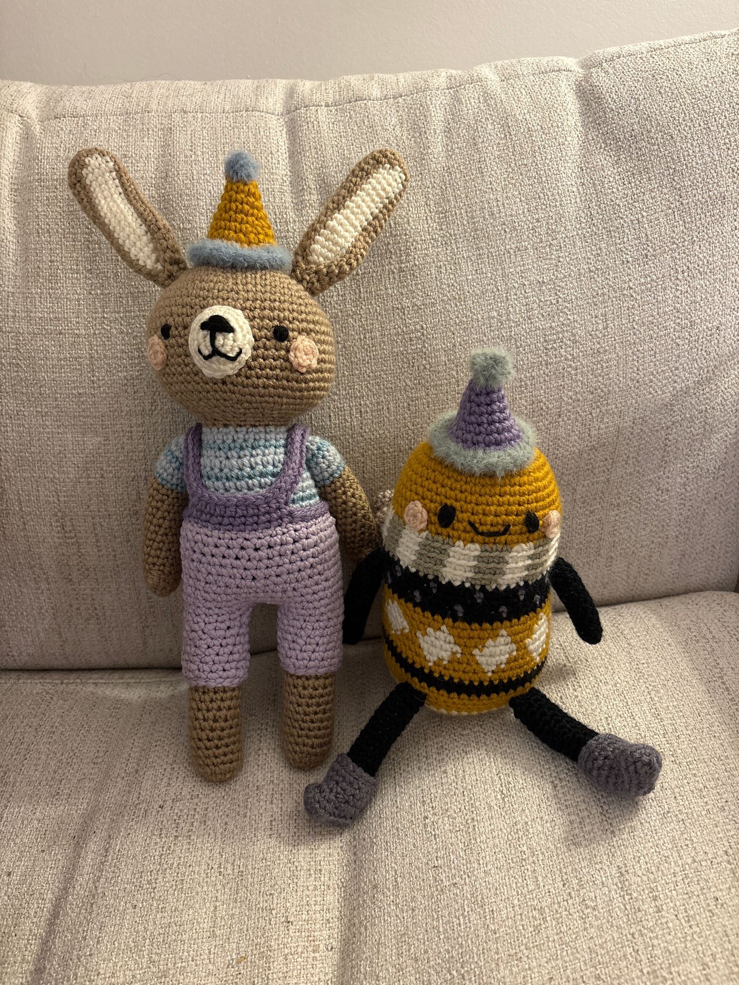 Two handmade crochet bunny and bee plush toys on a white couch.