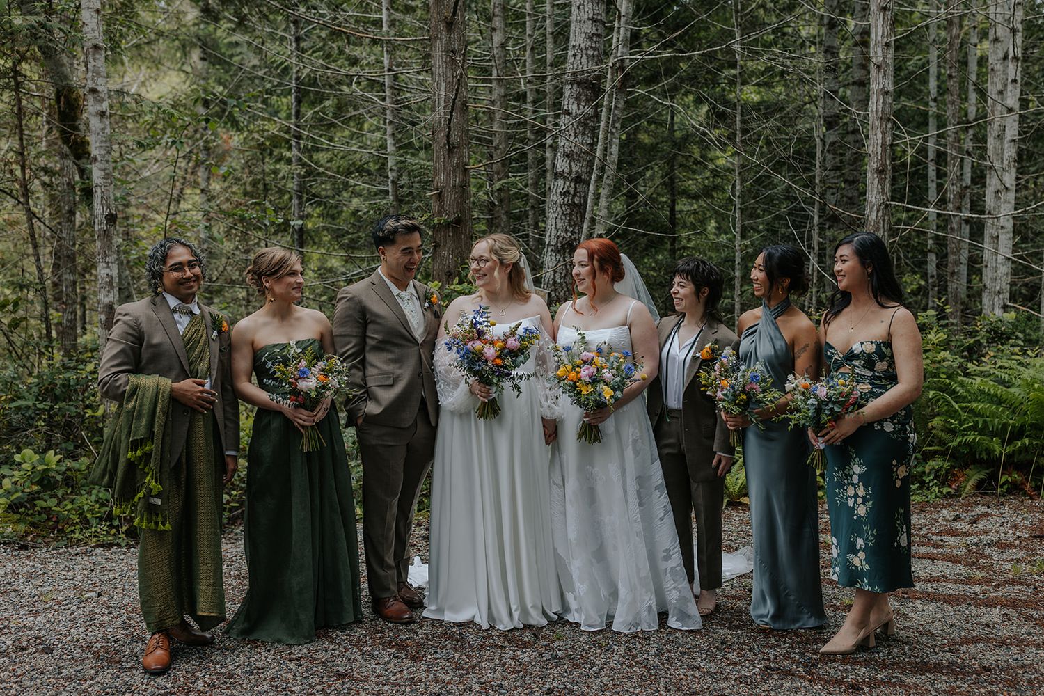 Wedding party members gathered outdoors among trees in green and white attire.