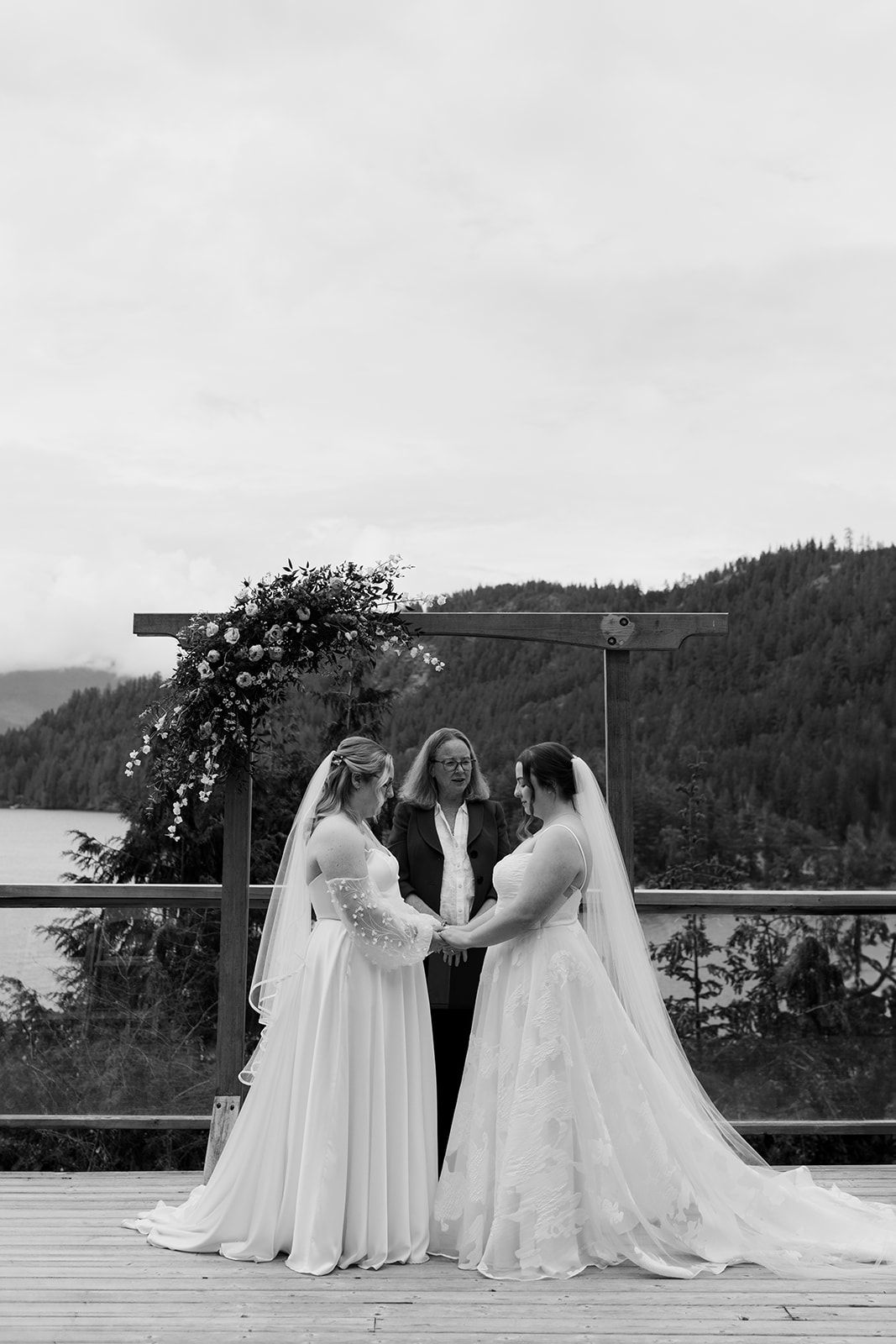 Black and white photo of brides in wedding dresses on scenic mountain deck.
