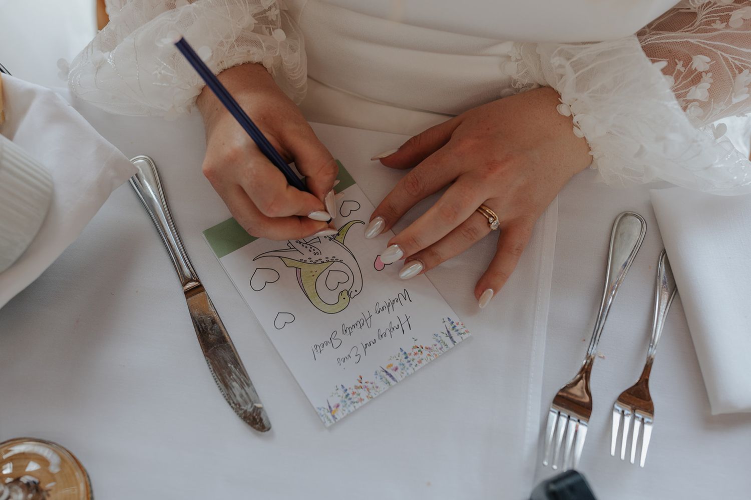 Close-up of hands drawing or writing on white paper with dining utensils nearby.