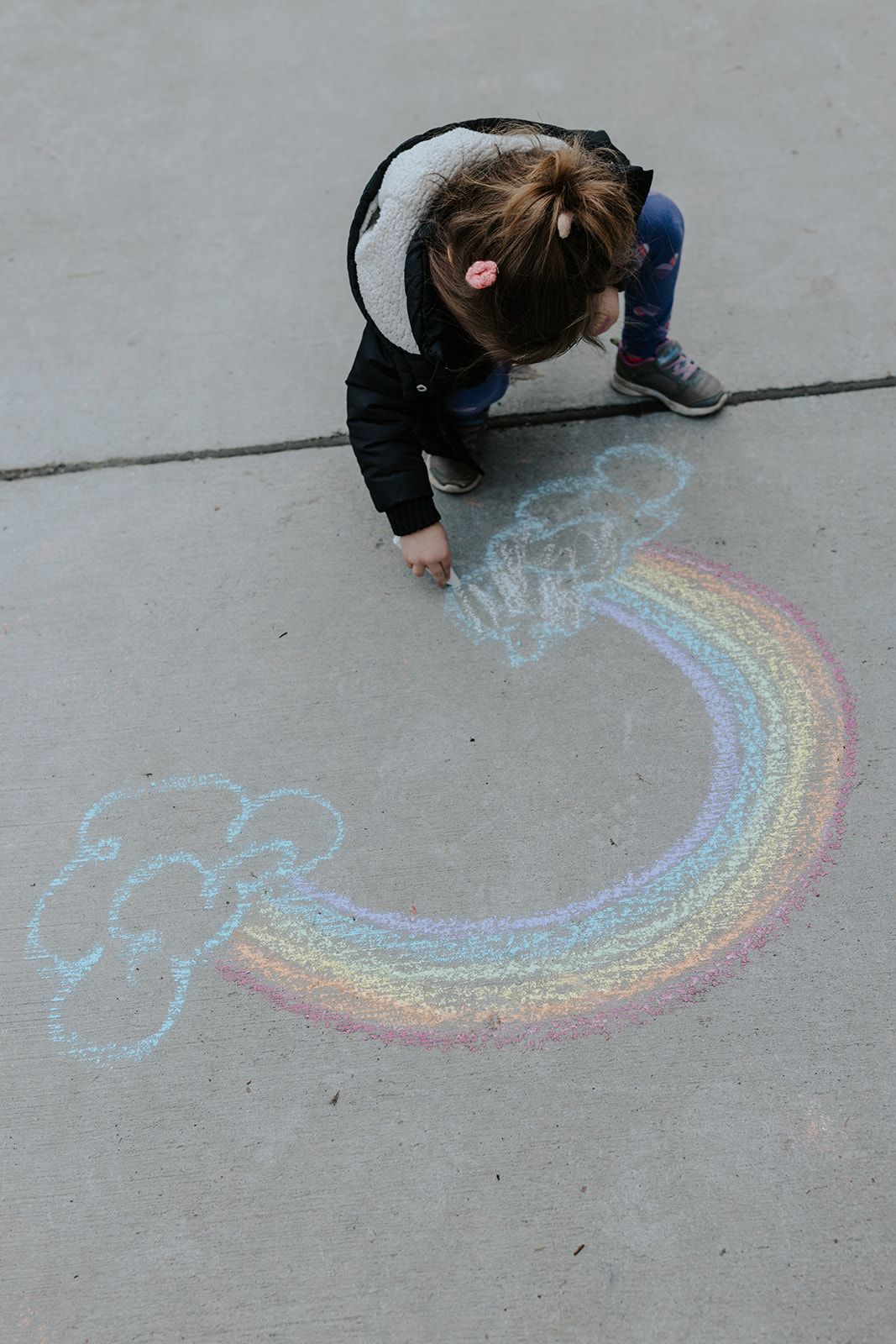 Person drawing a colorful rainbow with chalk on concrete ground.